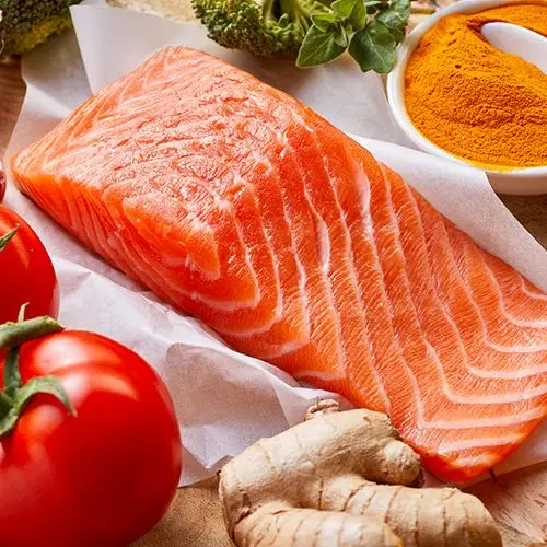 Nutrition for a healthy heart and cardiovascular system with fresh raw salmon rich in omega-3 fatty acids, tomatoes, turmeric, root ginger, stick cinnamon and garlic on a wooden table